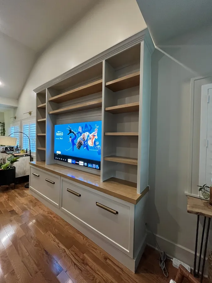 Two-tone built-in media wall with wood shelves and drawers, fitted under a vaulted ceiling