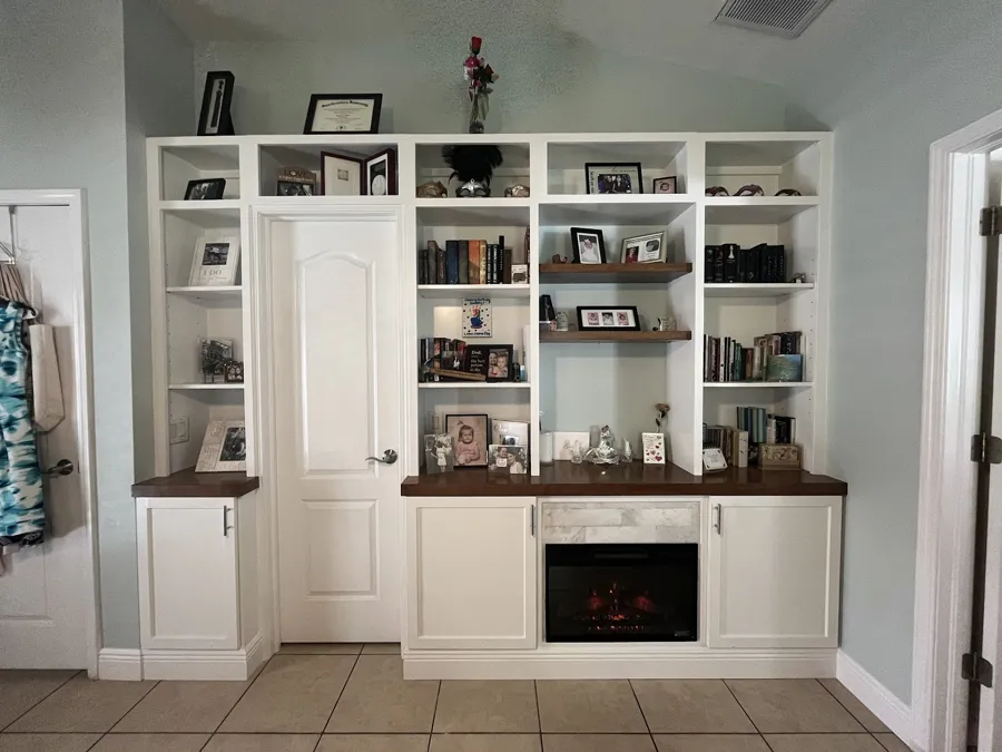 White built-in bookcase wall wrapped around a doorway, with a fireplace insert and a wood countertop
