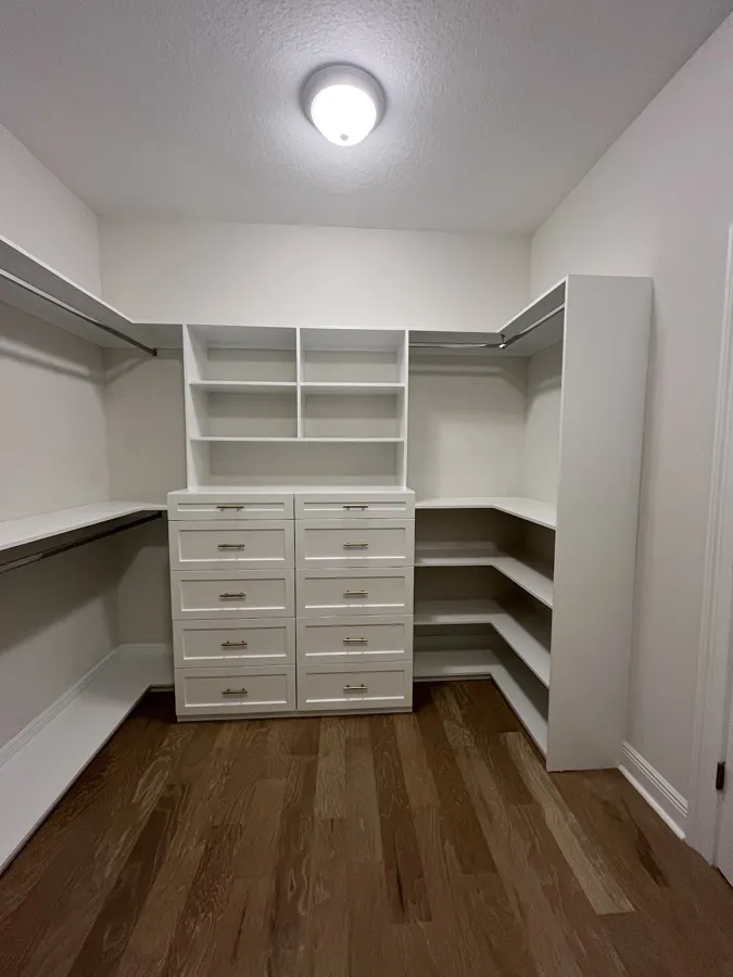 Custom walk-in closet with white drawers, shelves, and hanging rods